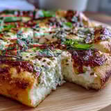 A close-up of Hot Honey Ricotta Pizza topped with fresh basil leaves, showcasing melted cheese and a vibrant, sweet-heat honey drizzle.