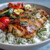 Sliced herb-roasted chicken breast over fluffy rice with roasted red peppers and zucchini, drizzled with a bright lemon dressing on top.