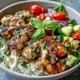 Savory Pesto Chicken Bowl featuring golden-brown chicken over rice, vibrant veggies, pine nuts, and fresh basil garnish, served warm.