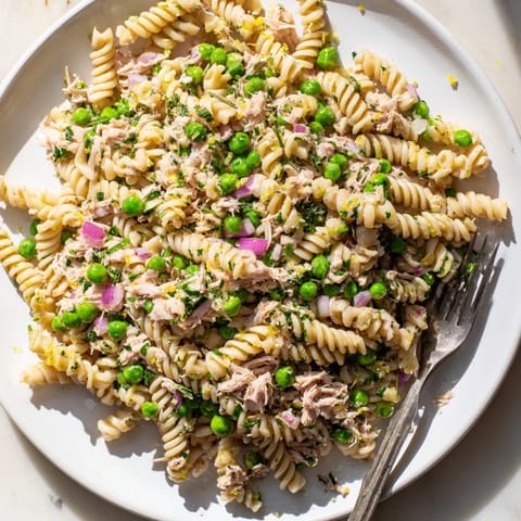 A vibrant bowl of Lemony Tuna Pasta Salad, featuring fusilli pasta, tender tuna flakes, bright green peas, and fresh herbs tossed in a zesty lemon dressing.  