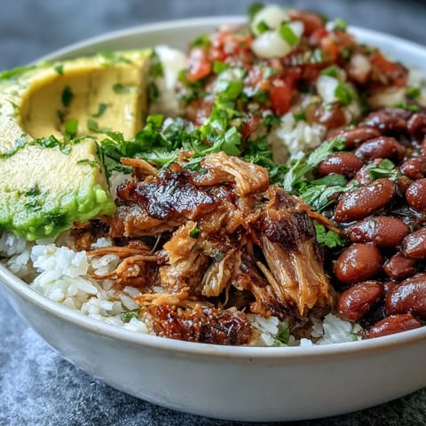 Shredded carnitas, pinto beans, and fresh salsa top a warm rice base in this delicious Carnitas Bowl.