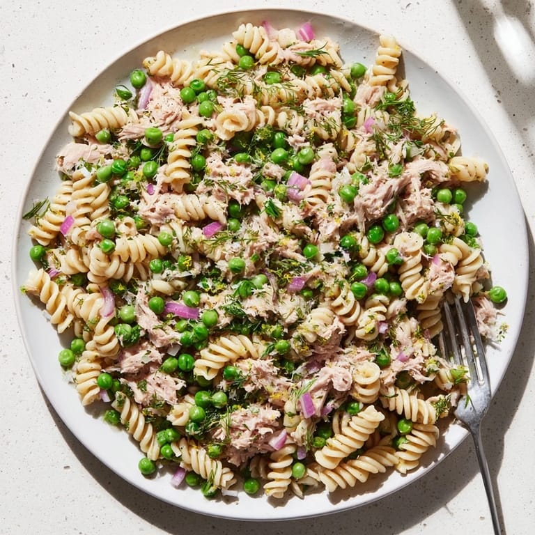 A close-up of Lemony Tuna Pasta Salad with colorful ingredients like red onion, peas, and tuna, showing the glossy olive oil and lemon juice coating the pasta.