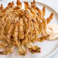 Crispy golden blooming onion, a deep-fried appetizer with a creamy, zesty dipping sauce.