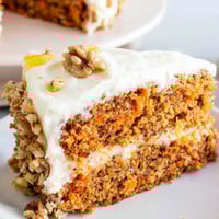 Moist carrot cake slice on a plate, frosted with creamy cheese, ready to eat now.