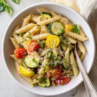 Penne pasta tossed with zucchini, yellow squash, and juicy cherry tomatoes in a garlic-basil sauce, garnished with Parmesan and lemon zest.  