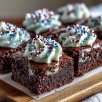 Festive firecracker brownie bites topped with creamy vanilla frosting and red, white, and blue sprinkles.  